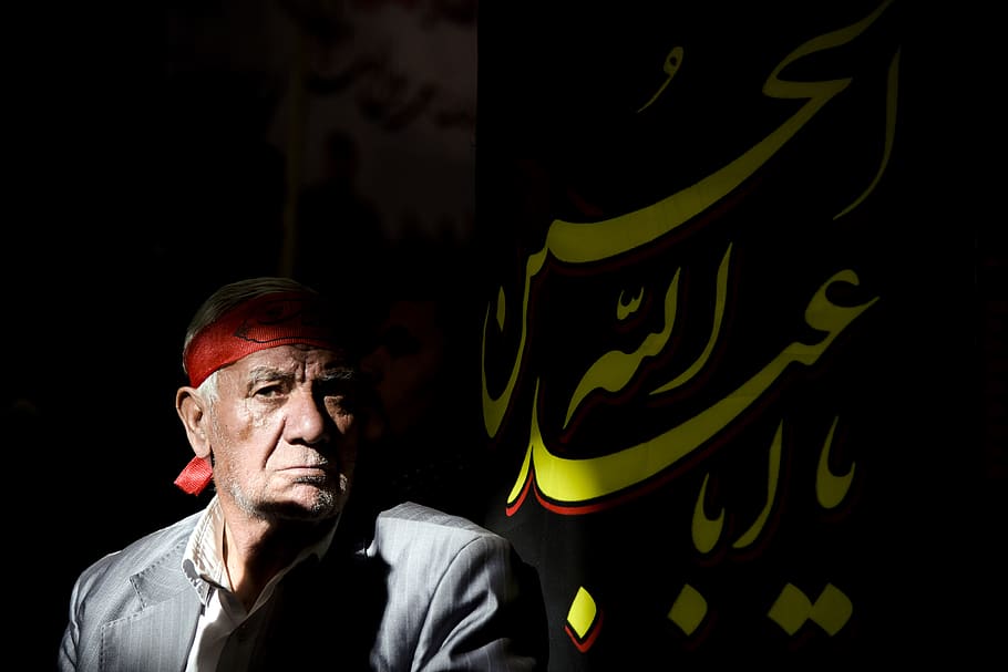 man in black jacket beside a flag with Arabic script text, eye HD wallpaper