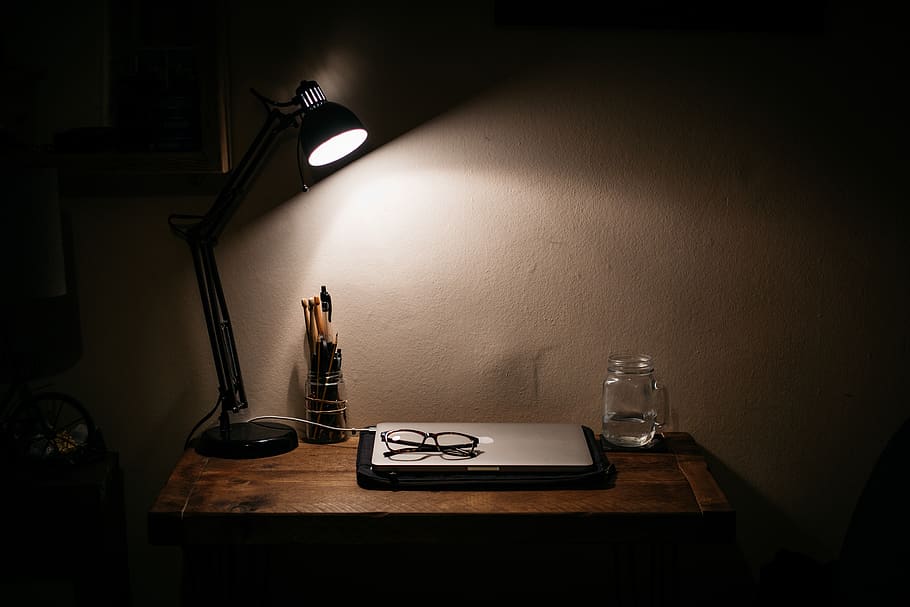 black desk lamp on brown wooden table, glasses, computer, water