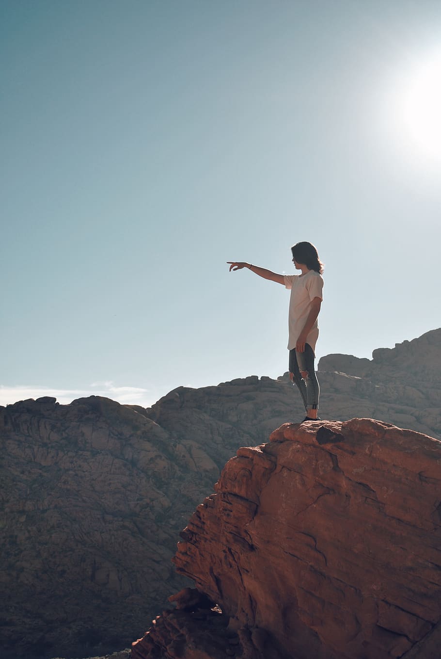 person in white shirt standing on mountain cliff pointing right finger during daytime