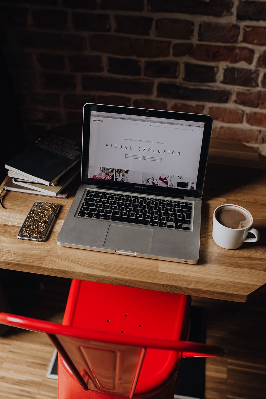Creatives desk with laptop, camera, journals and books in front of brick wall HD wallpaper