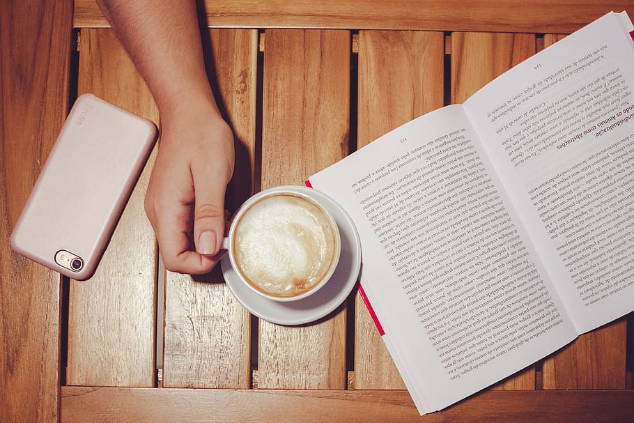 Person's Hand Holding White Coffee Mug With Plate on Brown Wooden Board With White and Black Book HD wallpaper