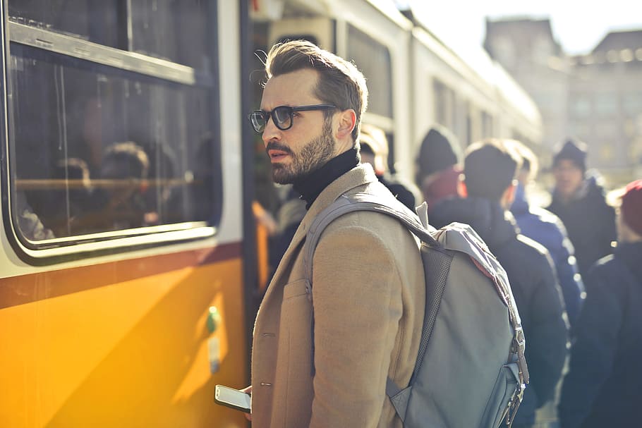 Handsome bearded male backpacker with backpack on his shoulders,waiting at the tram station