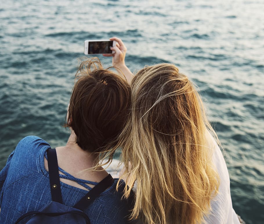 Two Women Sitting While Taking Picture Near Body of Water, adults