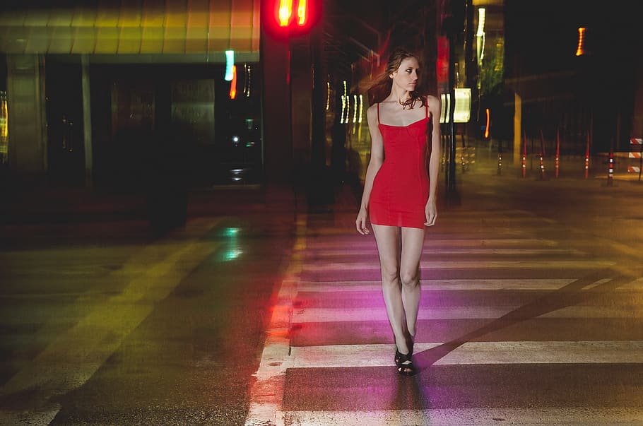 woman in red spaghetti strap midi dress walking on pedestrian lane during nighttime