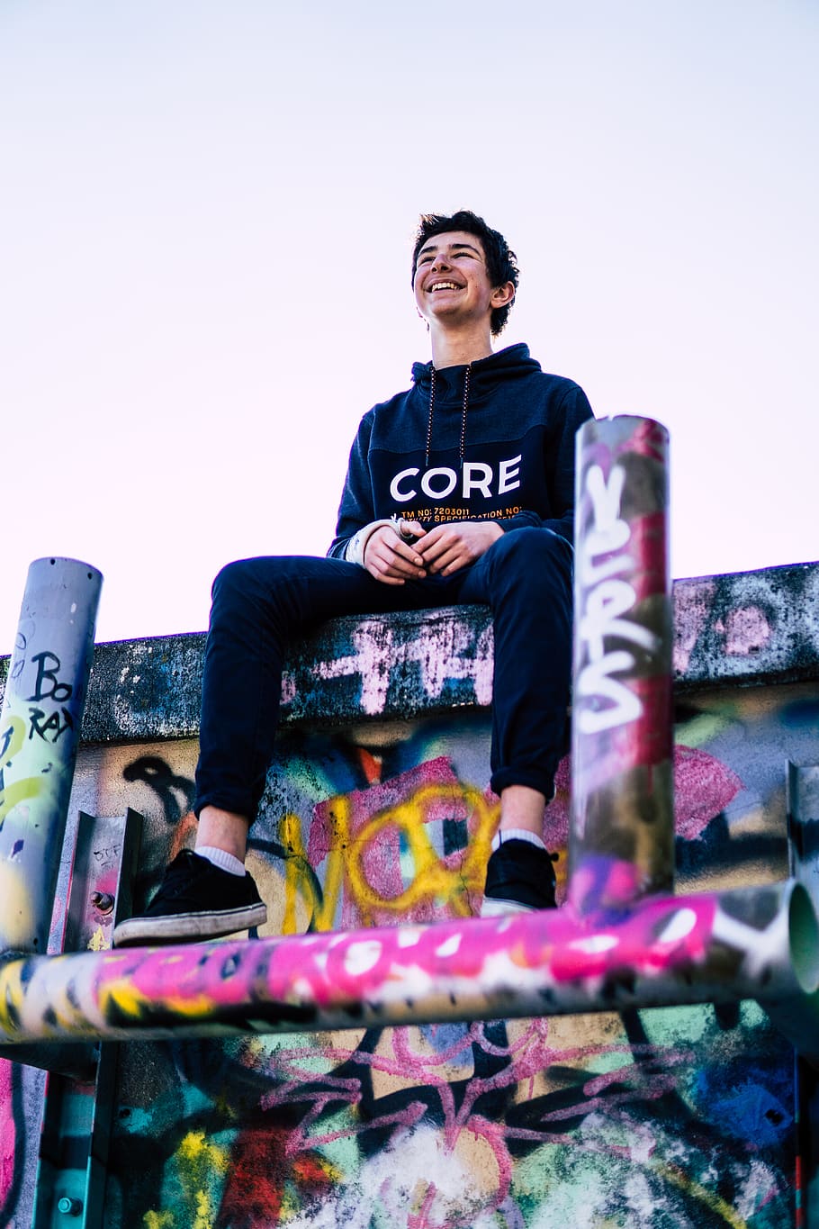 man sitting on wall with graffiti, apparel, clothing, human, person