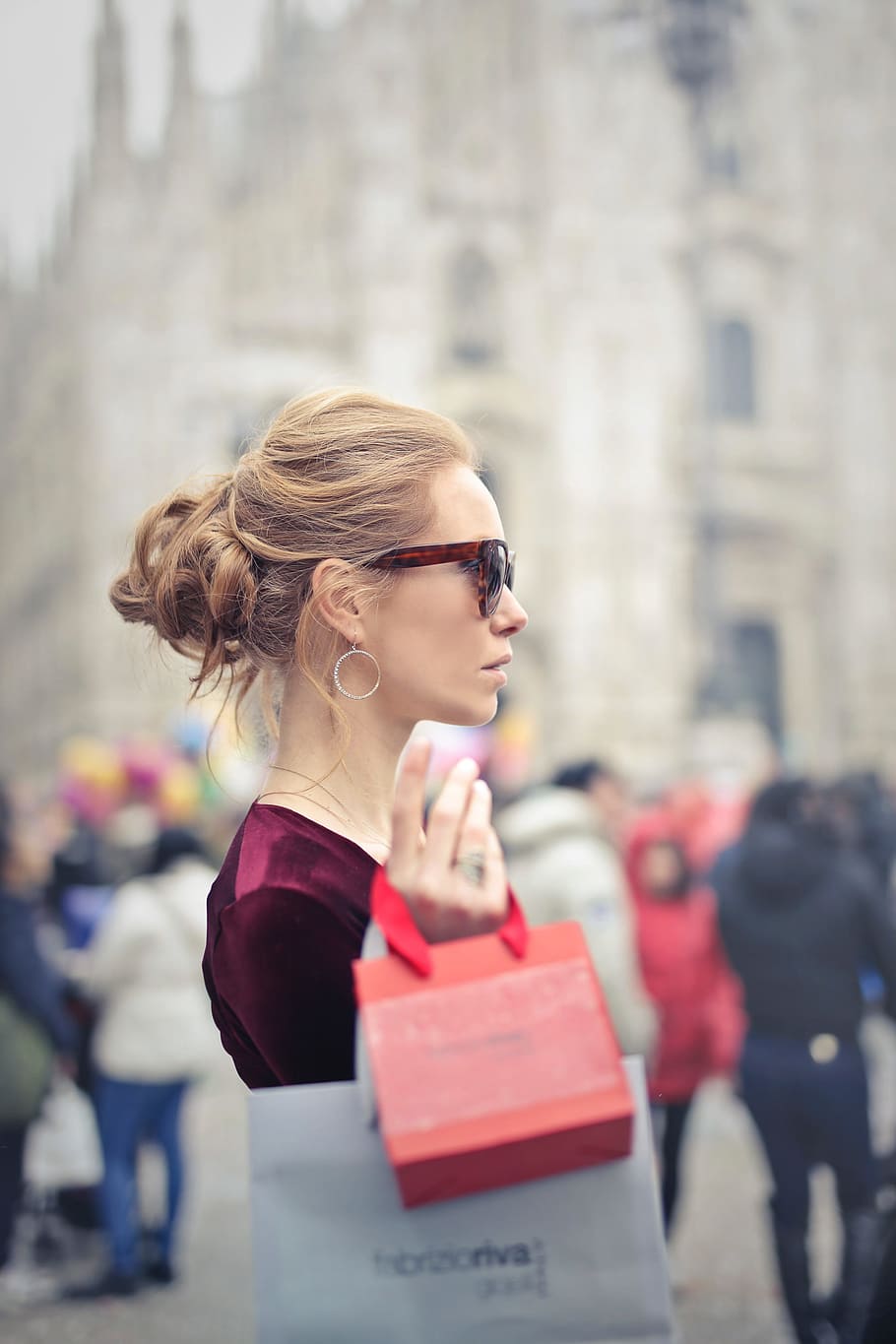 A young blonde woman with elegant hair bun holding shopping bags in her hand in outdoors