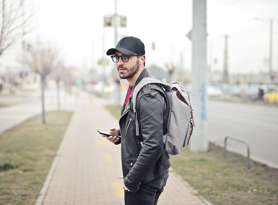 Young Adult bearded male backpacker with backpack on his shoulders seen listening to music in his cellphone