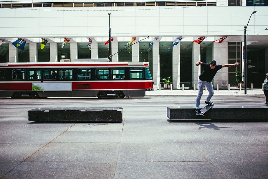 A young Caucasian skateboarder in action near a city building with a tram in the background
