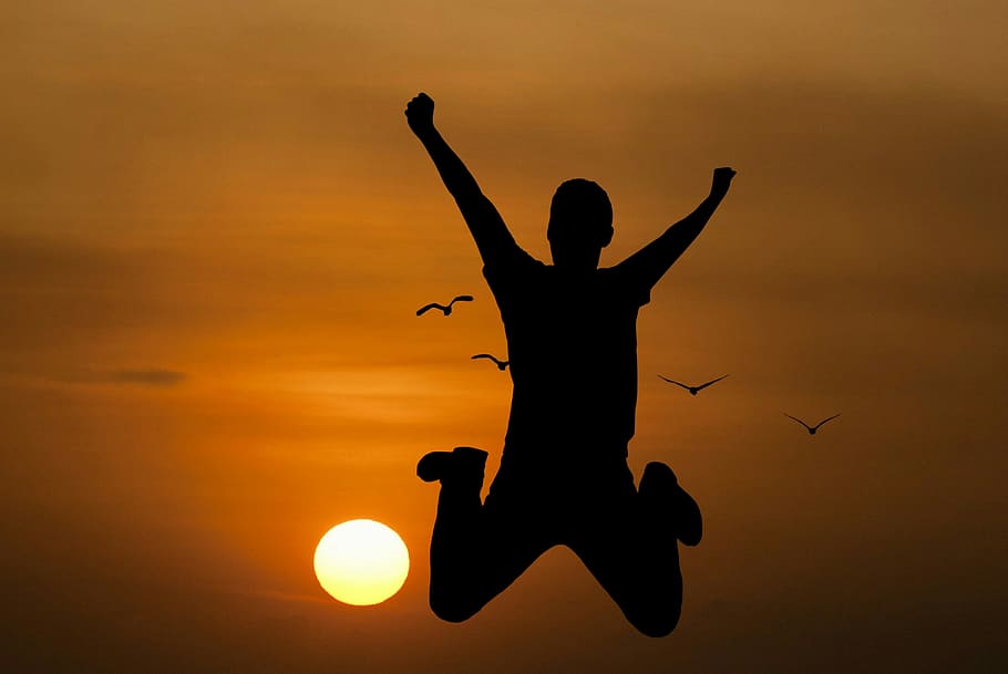 Silhouette of young man jumping with setting sun in background.