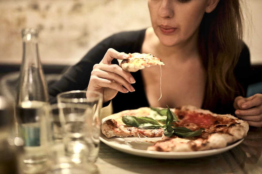 Woman Holds Sliced Pizza Seats by Table With Glass, blow, cheese