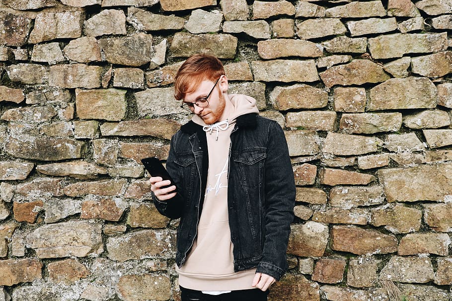 man looking down while holding smartphone, wall, coat, jacket HD wallpaper