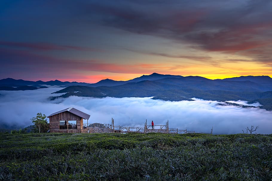Brown Wooden House Near Green Field and Mountain View Under Orange and Yellow Skies HD wallpaper