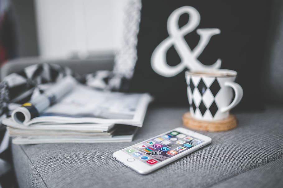 White mobile phone lying on a couch with cup and stack of magazines HD wallpaper