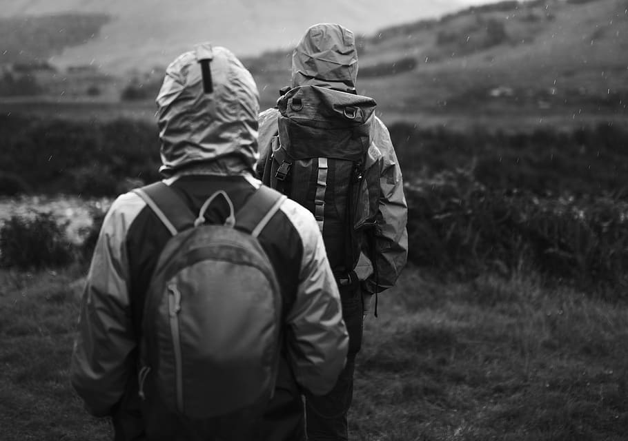 Two People With Backpacks Hiking on Green Field Greyscale Photography HD wallpaper