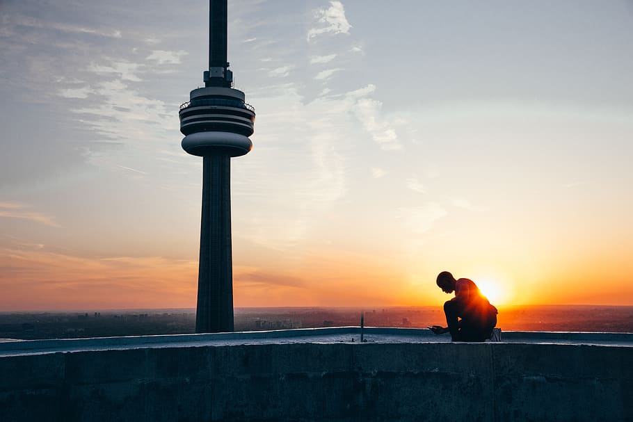 Silhouette of a Man Sitting Near Black Tower Near Body of Water during Sunset HD wallpaper