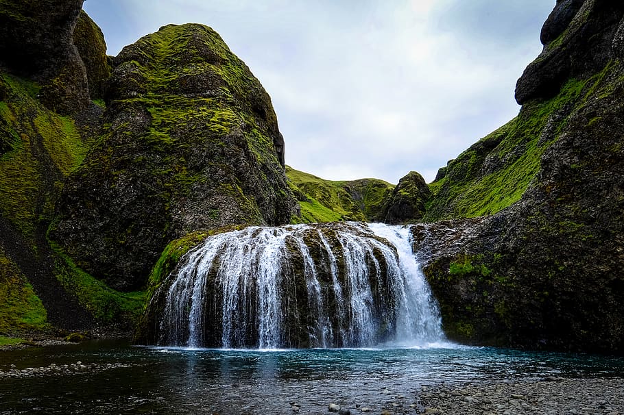 waterfalls near grass mountain range, outdoors, river, cliff