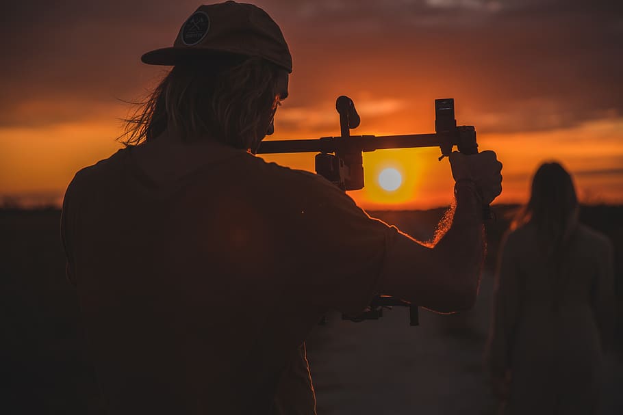 man holding camera stick, human, person, outdoors, sunrise, sunset HD wallpaper