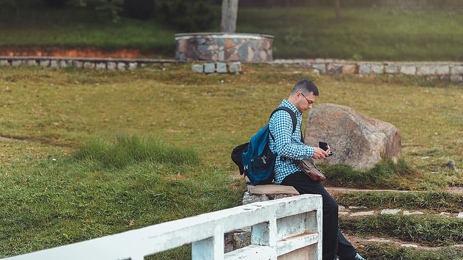 Man Sitting on White Railing Near Rock, backpack, cellphone, daylight HD wallpaper