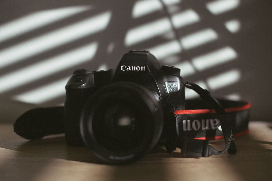 black Canon DSLR camera on wooden surface, electronics, strap