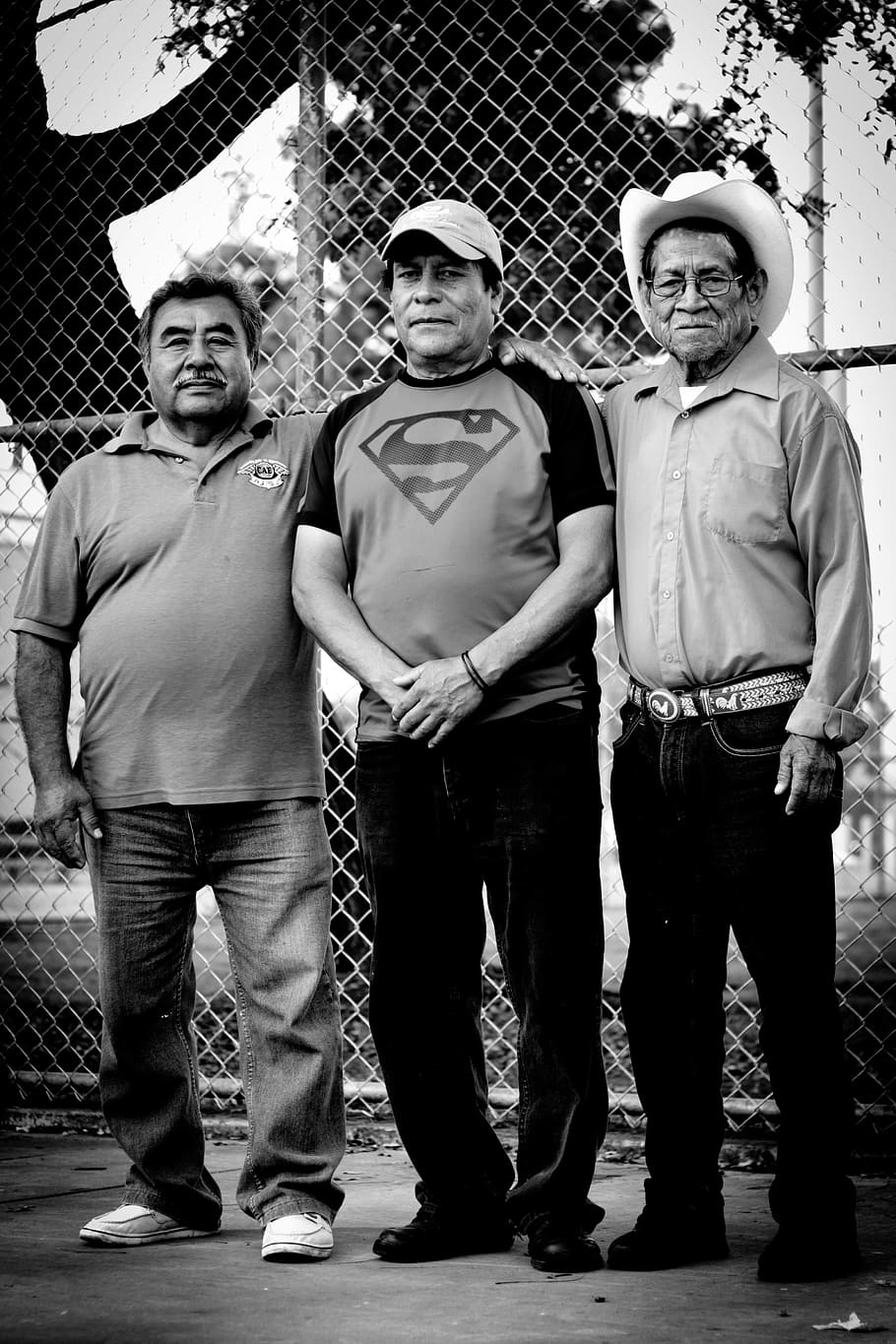 grayscale photography of three men standing near chain link fence