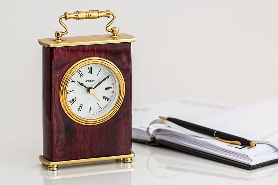 Brown and Brass-colored Desk Clock on White Surface Beside Black Click Pen on Opened Notebook HD wallpaper