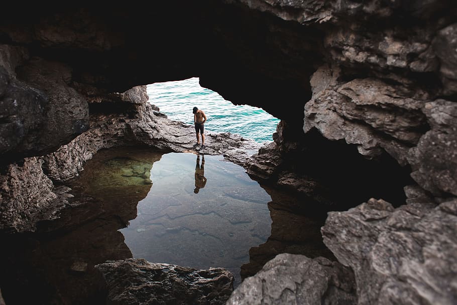 An explorer looks at his reflection in still water in an open cave near a body of water