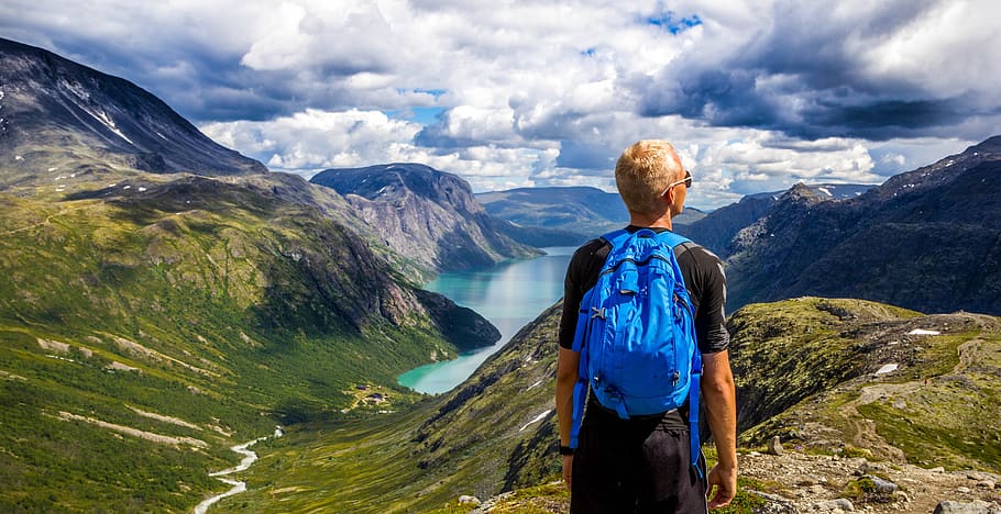 Man Standing on Mountain Cliff Facing Body of Water Between Mountain HD wallpaper