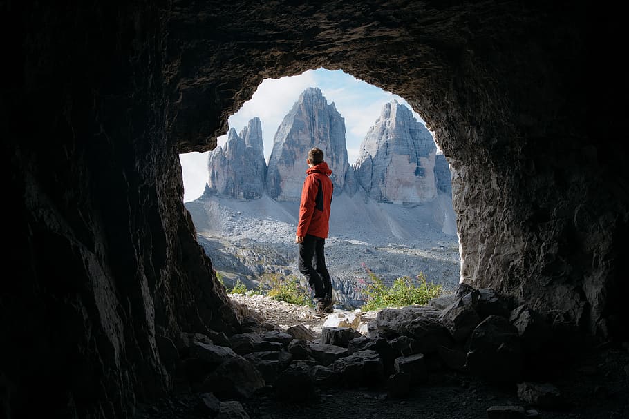 Man in Red Jacket Standing Outside of Cave in Front of Three Mountains, HD wallpaper