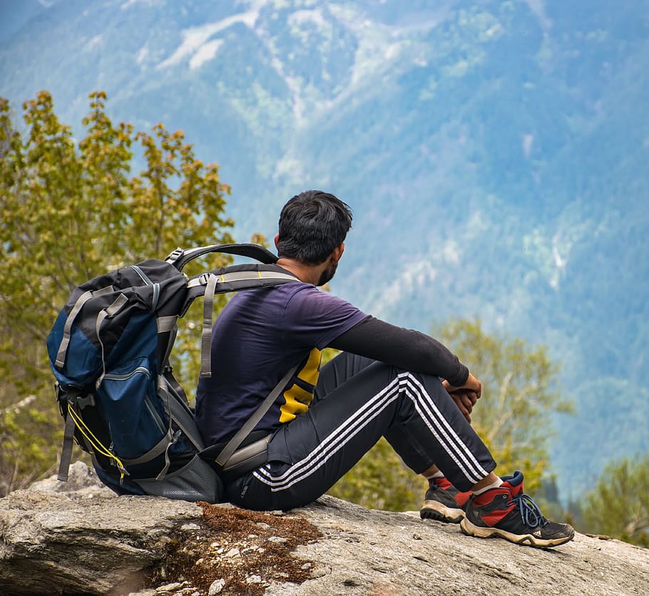 Man in Purple T-shirt With Blue Backpack Sitting on Gray Boulder HD wallpaper