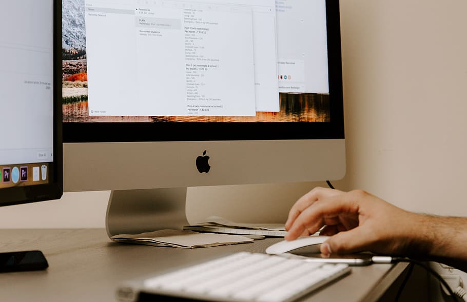 person holding white Apple Magic Mouse beside iMac and keyboard HD wallpaper