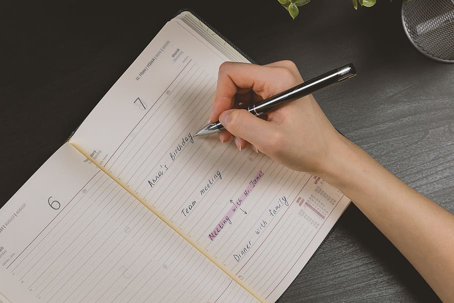 The woman’s hand holds a pencil and writes a plan into a diary in the office HD wallpaper