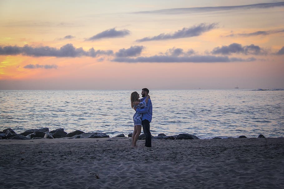 Couple Face to Face Stands on Seashore Near Calm Water during Golden Hour HD wallpaper