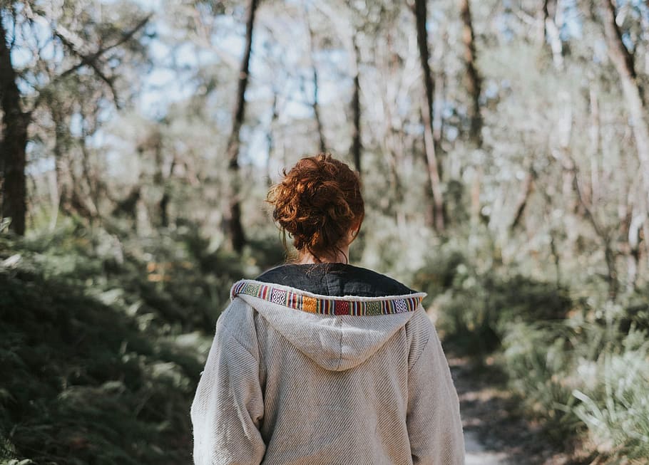 selective focus photography of woman wearing hoodie standing on ground surrounded with trees HD wallpaper