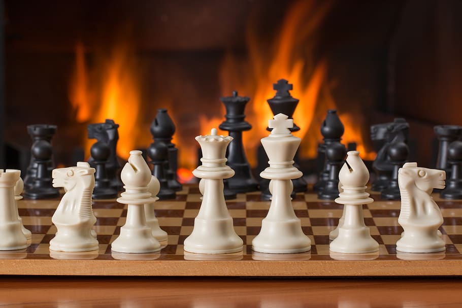 White and Black Chess Pieces on Board in Front of Fireplace, battle