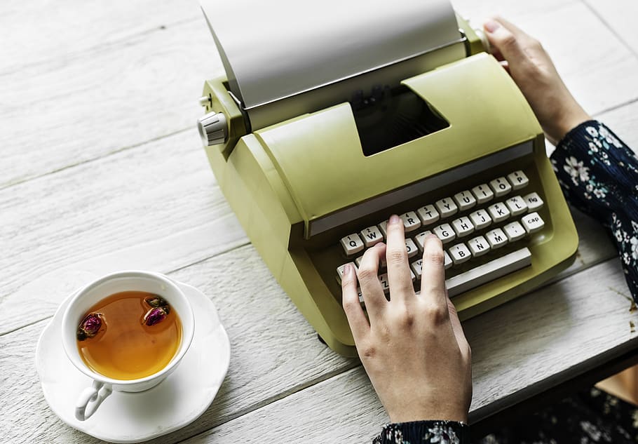 Person Holding Type Writer Beside Teacup and Saucer on Table HD wallpaper