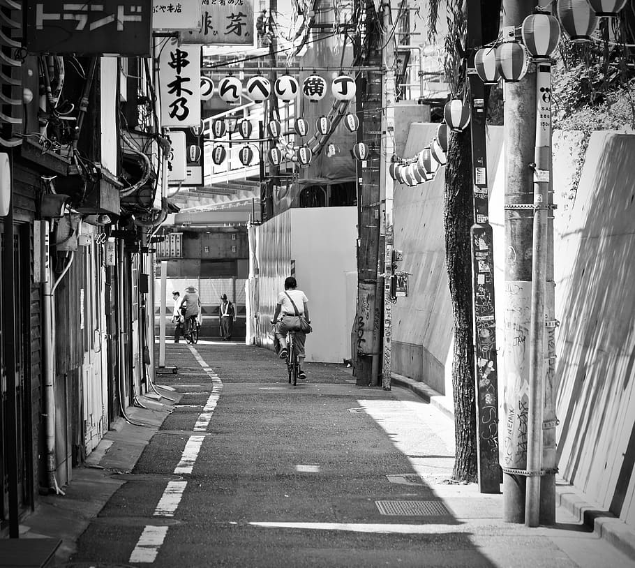 grayscale photo of man riding bike, street, urban, city, alley