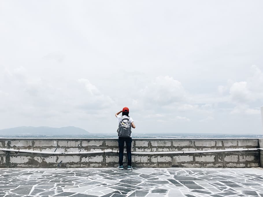 Man Standing Near Grey Wall, backpacker, beach, clear sky, from behind HD wallpaper