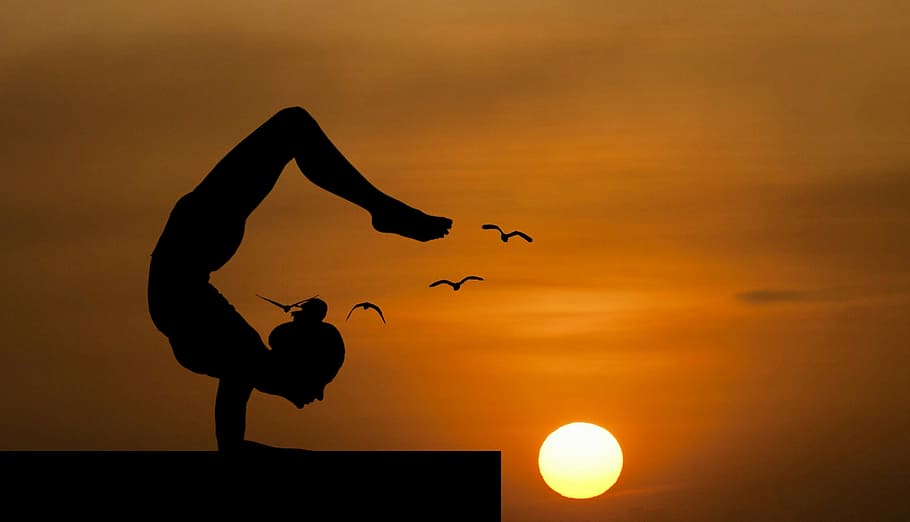 Woman doing an acrobatic yoga pose, silhouetted against sunset.