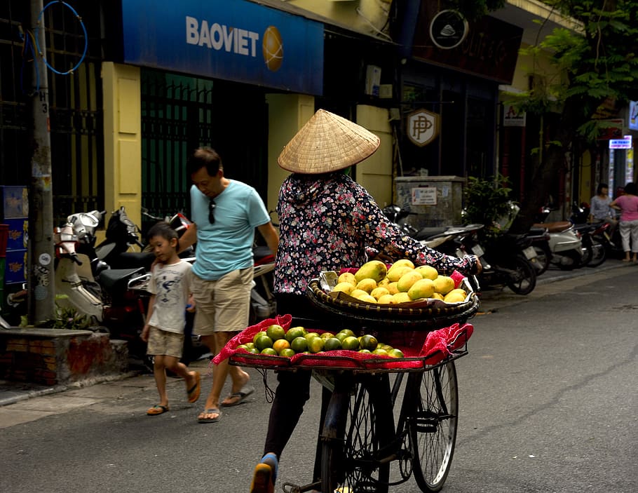 woman holding bicycle near Baomet storefront, human, person, citrus fruit