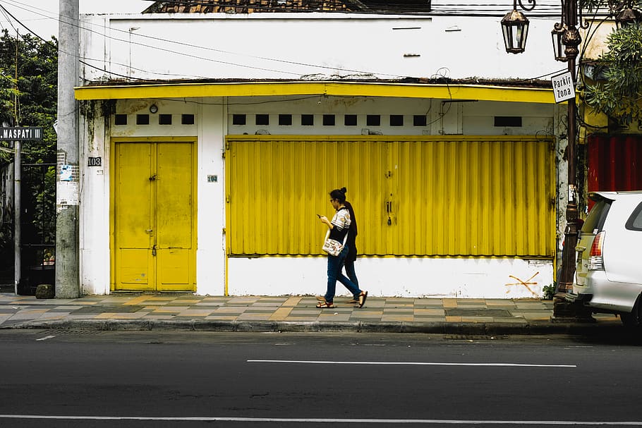 woman walking on sidewalk beside yellow and white house, shoe