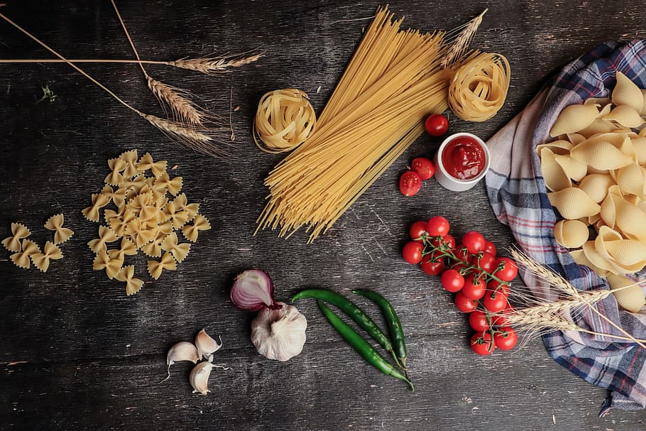 flatlay photo of pasta noodles, tomatoes, tomato sauce, onions, and garlic