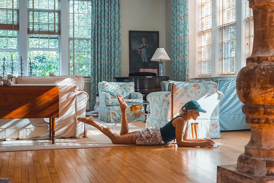 woman lying on brown floor near blue and white sofa set inside white room with glass windows at daytime, HD wallpaper