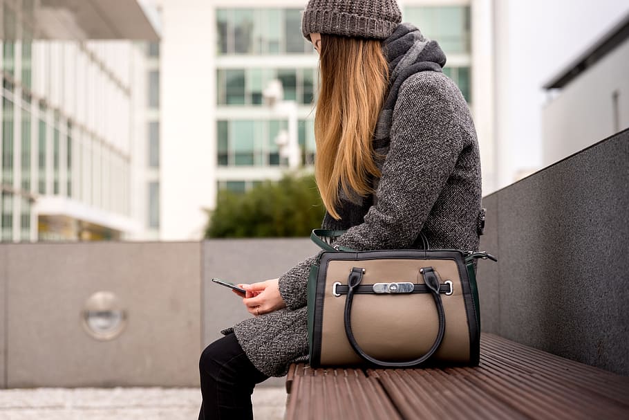 woman sitting on bench outside and using smartphone, one person HD wallpaper