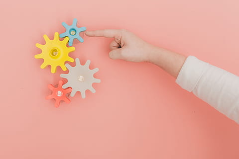 Finger turning colorful toy gears on peach color wall, mechanical HD wallpaper