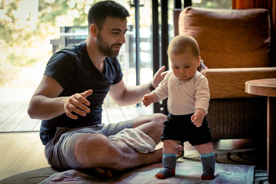 A man helping teach his 1 year old how to walk., first steps
