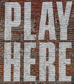 Large painted letters say PLAY HERE in white on an old red brick wall. HD wallpaper