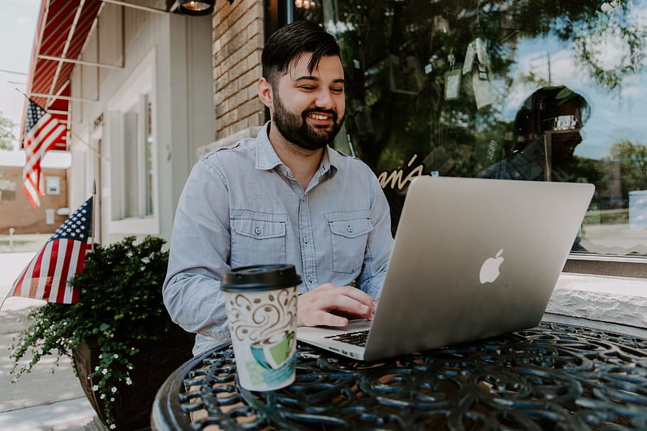 man in gray denim dress shirt smiling while using MacBook Pro HD wallpaper