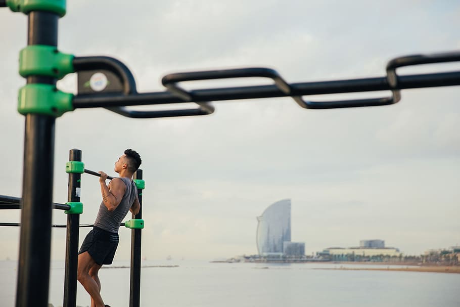 A young Asian man doing chin-up exercise on the beach, Adult